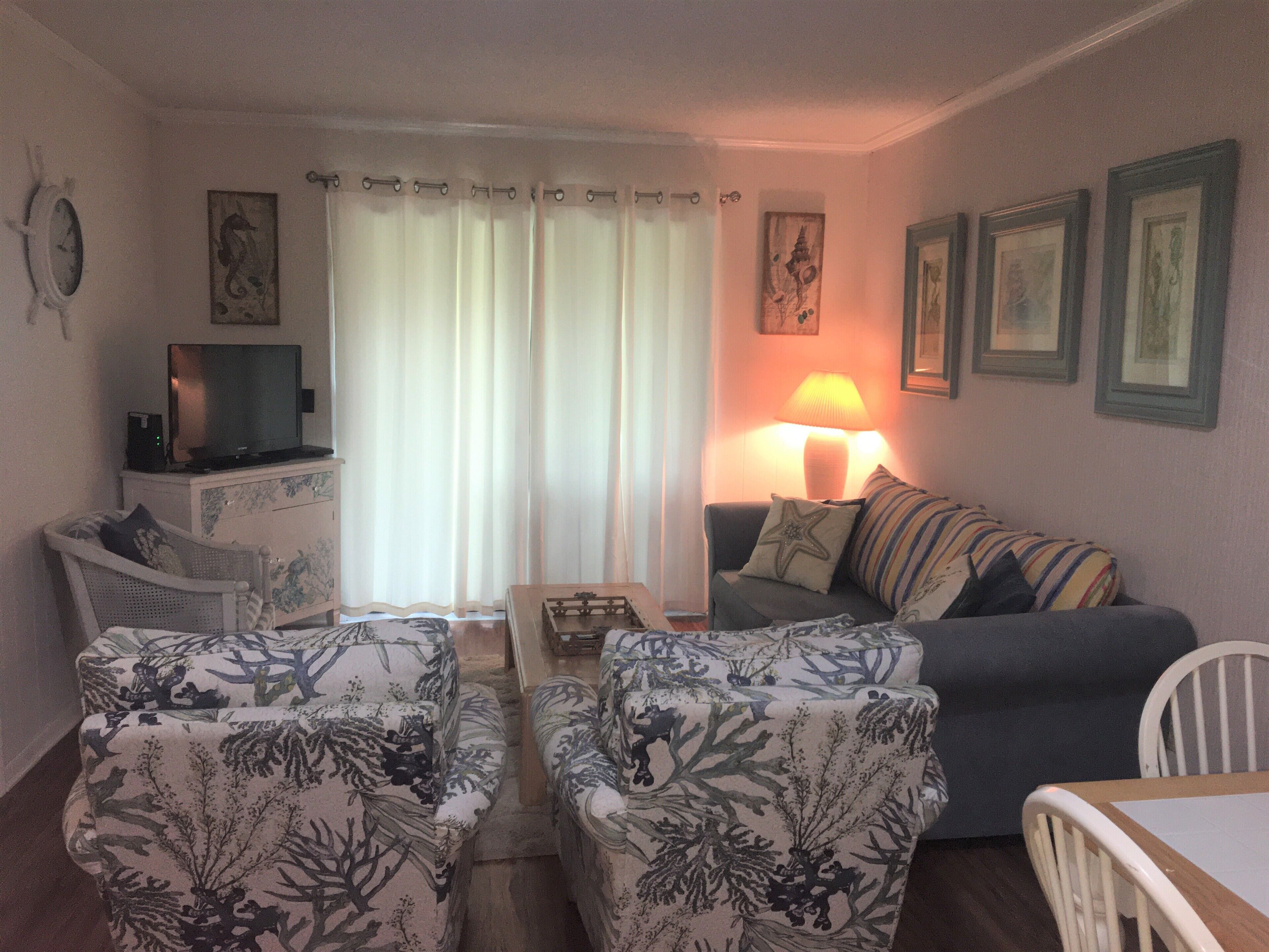 A living room with a sofa, two armchairs, a television, a lamp, and a small table.