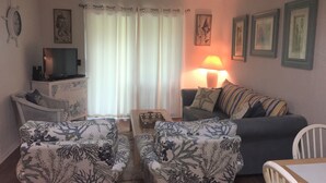 Ein Wohnzimmer mit einer Couch, zwei Sesseln, einem Fernseher, einer Lampe und einem kleinen Tisch.