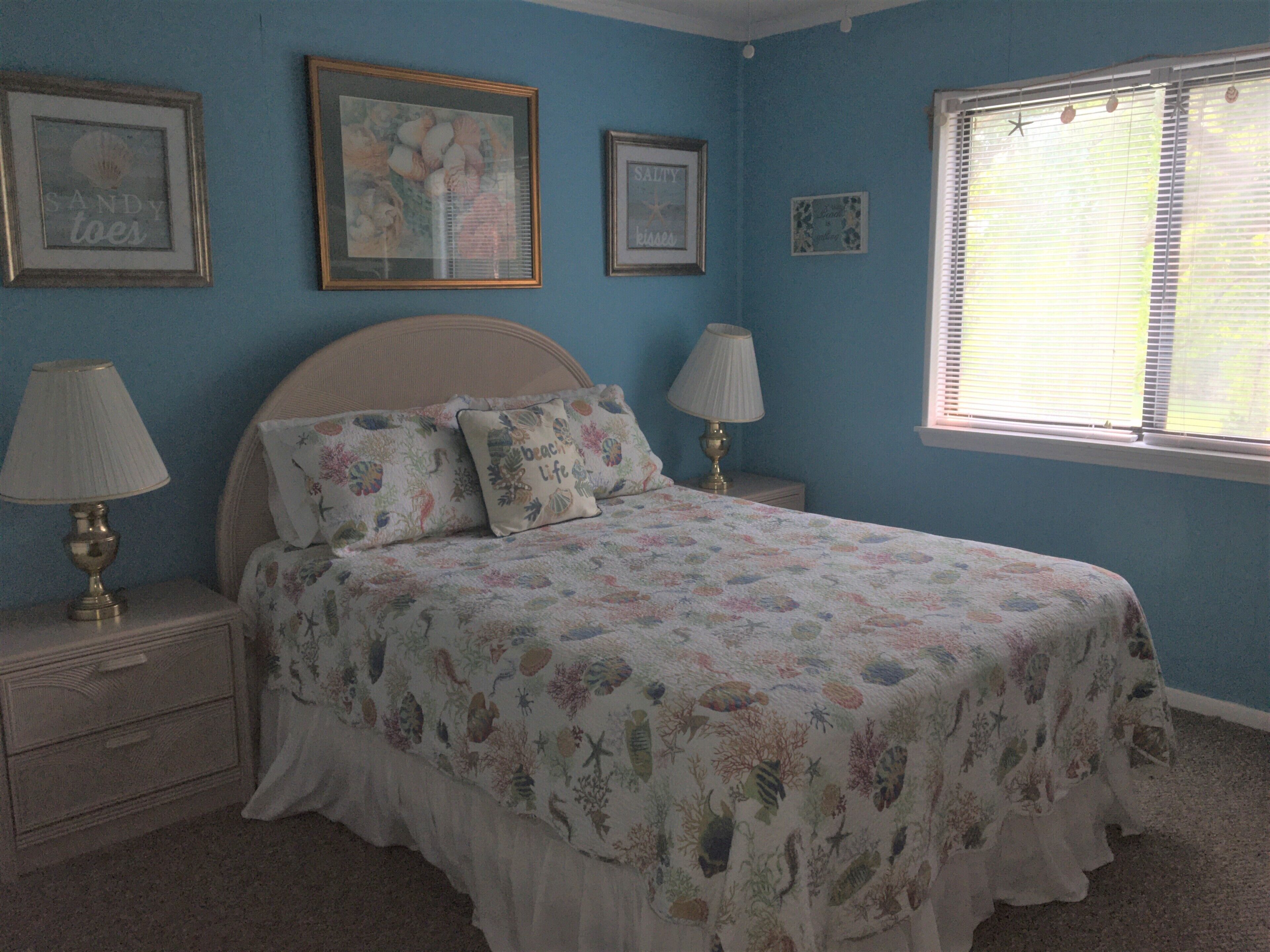 A bedroom with a bed, two bedside tables, a nightstand, and a window with blinds.