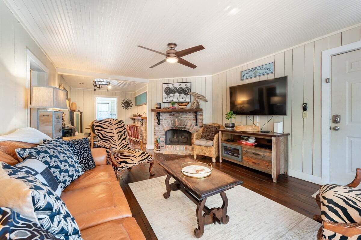 A cozy living room with a sofa, armchairs, a fireplace, a television, and a ceiling fan.