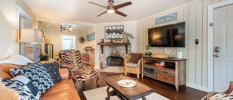 A cozy living room with a sofa, armchairs, a fireplace, a television, and a ceiling fan.