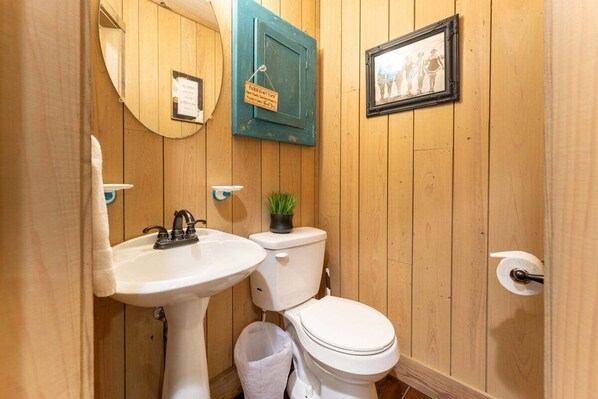 A wooden-paneled bathroom with a white sink, toilet, and a small potted plant.