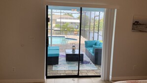 Quarto com porta de correr de vidro que dá para um pátio com piscina, móveis de exterior e vista para uma casa e para a água.