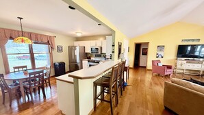 A spacious living area with a kitchen, dining table, and a sofa. - Beautiful, Cedar Lakeside Cabin with Private Dock (Cadiz)