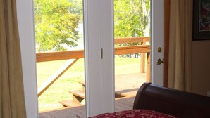 A bedroom with a bed, a wooden deck, and a view of a grassy area and trees. - Beautiful, Cedar Lakeside Cabin with Private Dock (Cadiz)