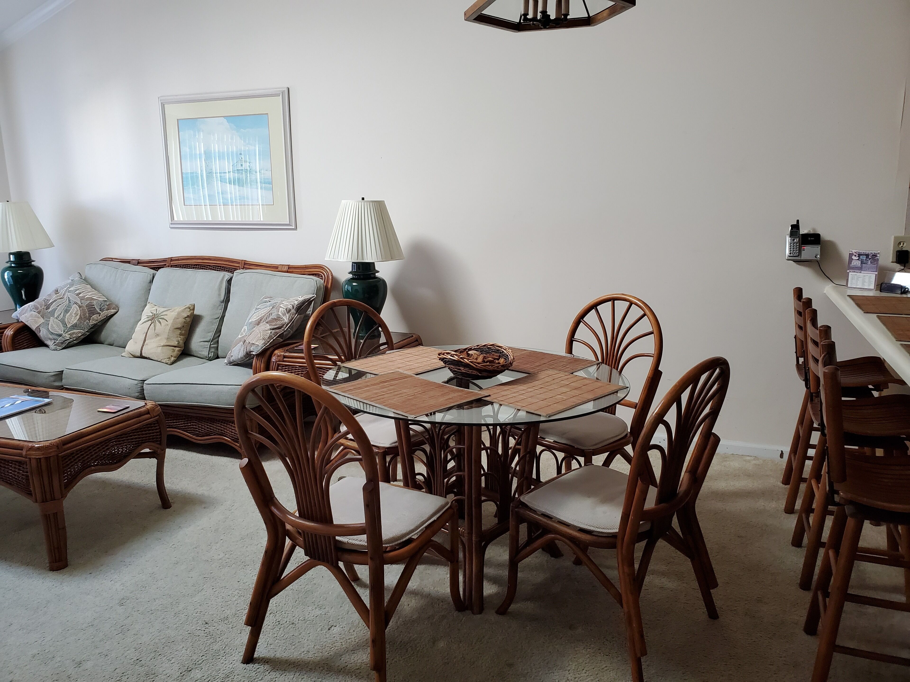 A living room with a round glass table, wicker chairs, a sofa, and a framed picture on the wall.