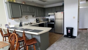 A kitchen with a central island, wooden chairs, a refrigerator, a microwave, and a coffee maker. - Beautiful 2 Bedroom, 2 Bath Ocean View Condo in Surfside Beach (Surfside Beach)