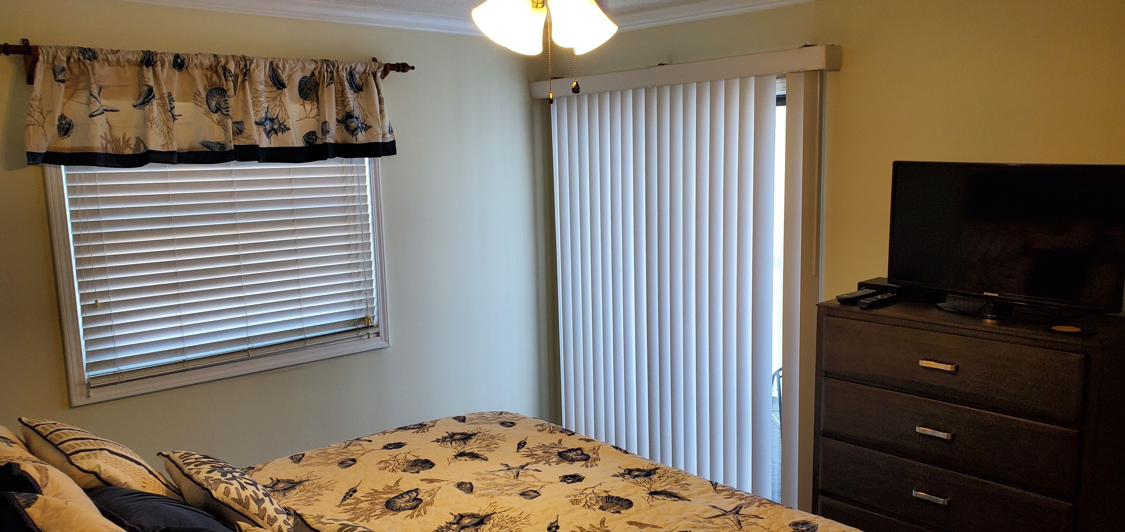 A bedroom with a bed, a dresser, a television, and a window with blinds.