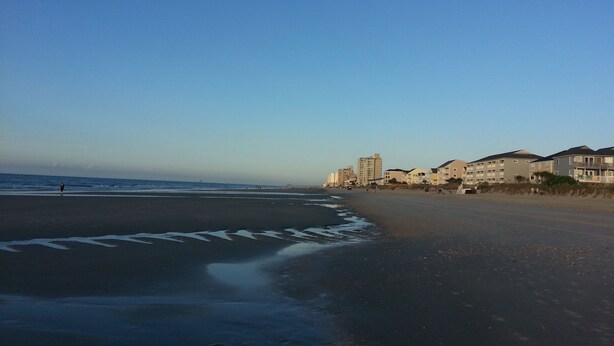 A beach with a clear sky, a sandy shore, and buildings in the background. - Beautiful 2 Bedroom, 2 Bath Ocean View Condo in Surfside Beach (Surfside Beach)
