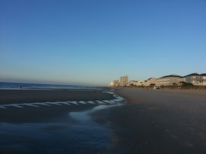 A beach with a clear sky, a sandy shore, and buildings in the background.