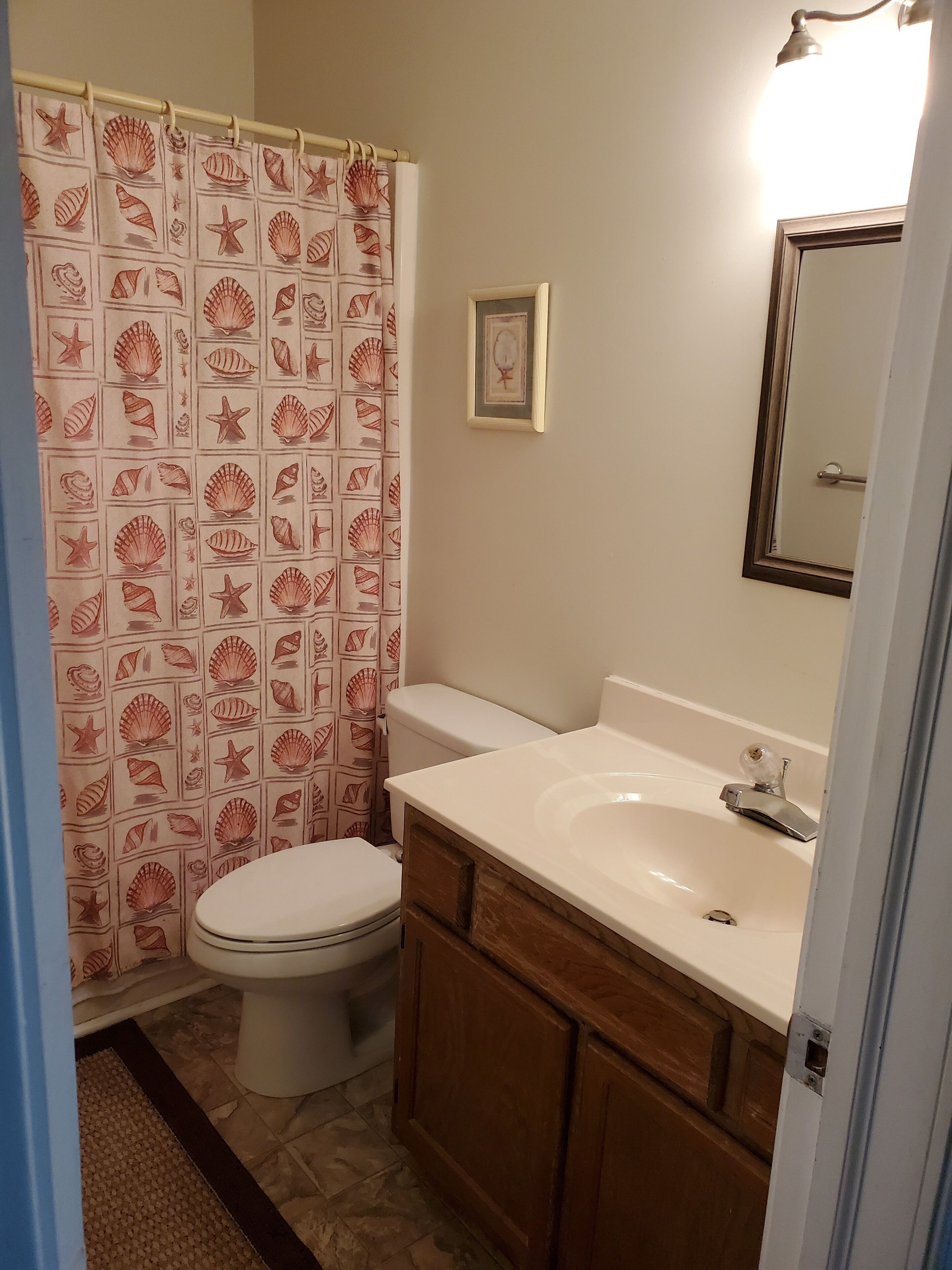 Un baño con inodoro, lavamanos y cortina de ducha con estampado de conchas marinas.