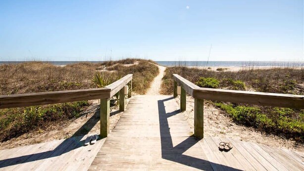Un paseo marítimo de madera que conduce a una playa, con cielo despejado.