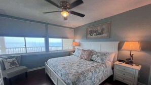 Un dormitorio con cama, mesita de noche, banco, ventilador de techo y ventana con vistas.