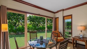 A room with a glass table, wooden chairs, a lamp, and a view of a green garden through large windows. - Waipouli Beach Resort - Ground Floor #E103,  2 King Masters Suites (Kapaa)