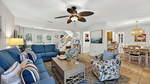 Un salon spacieux avec un canapé bleu, un fauteuil à motifs, une table basse en bois et un ventilateur de plafond.