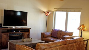 Ein Wohnzimmer mit Holzboden, einem Flachbildfernseher, Ledersofas, einem Couchtisch und einer Lampe.