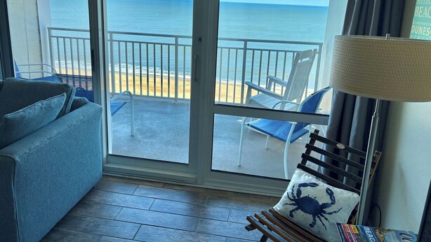 A room with a view of the beach, a sofa, a chair, and a lamp. - Carousel Oceanfront Condo w/ Stunning Ocean & Bay Views! (Ocean City)