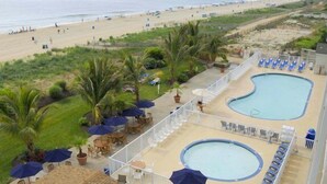 A poolside area with lounge chairs and umbrellas, a pool, and a view of the beach. - Carousel Oceanfront Condo w/ Stunning Ocean & Bay Views! (Ocean City)