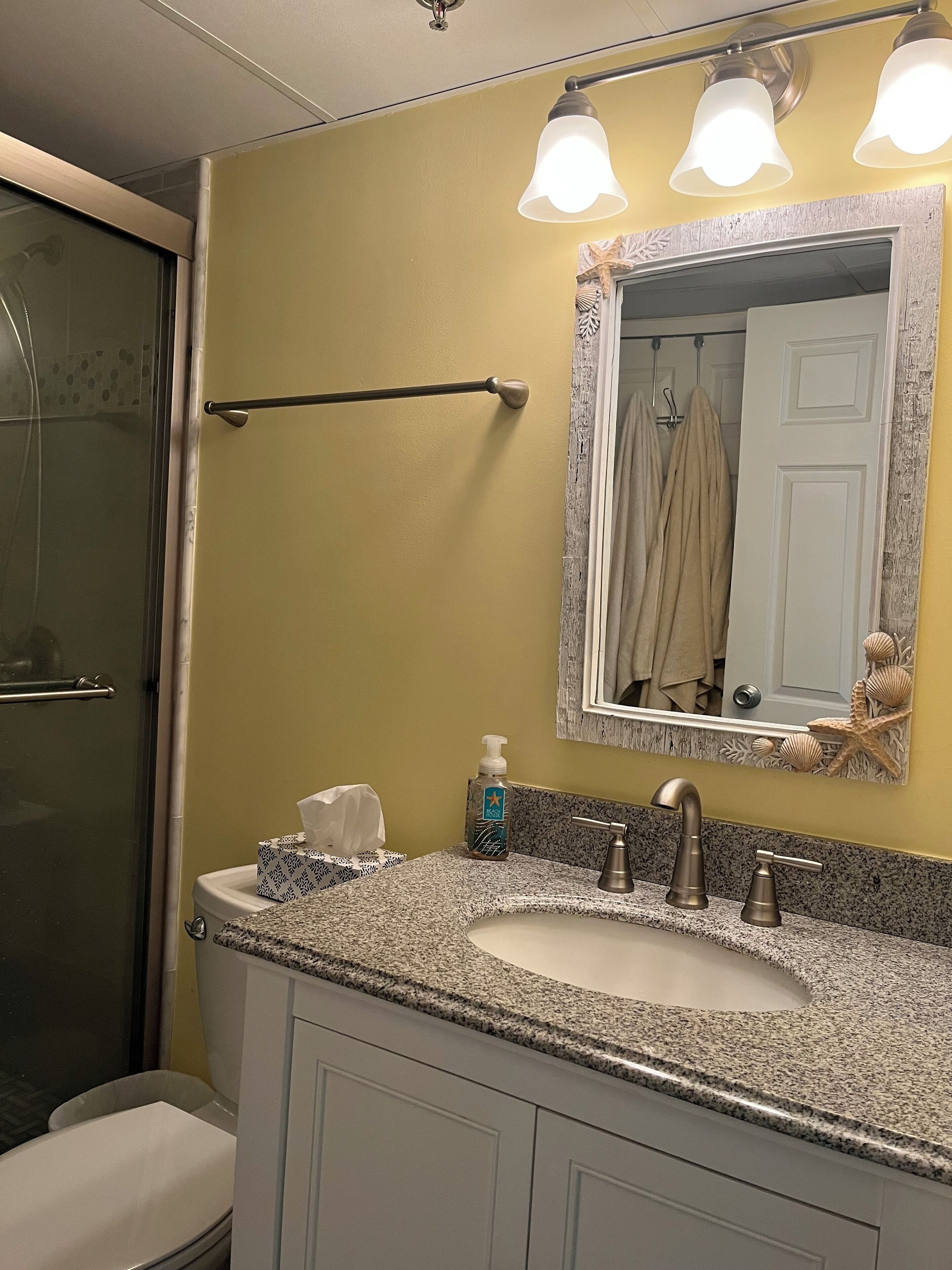Une salle de bain dotée d’un comptoir en granit, d’un lavabo blanc, d’un miroir avec un cadre décoratif et d’un porte-serviettes sur lequel est posée une serviette.