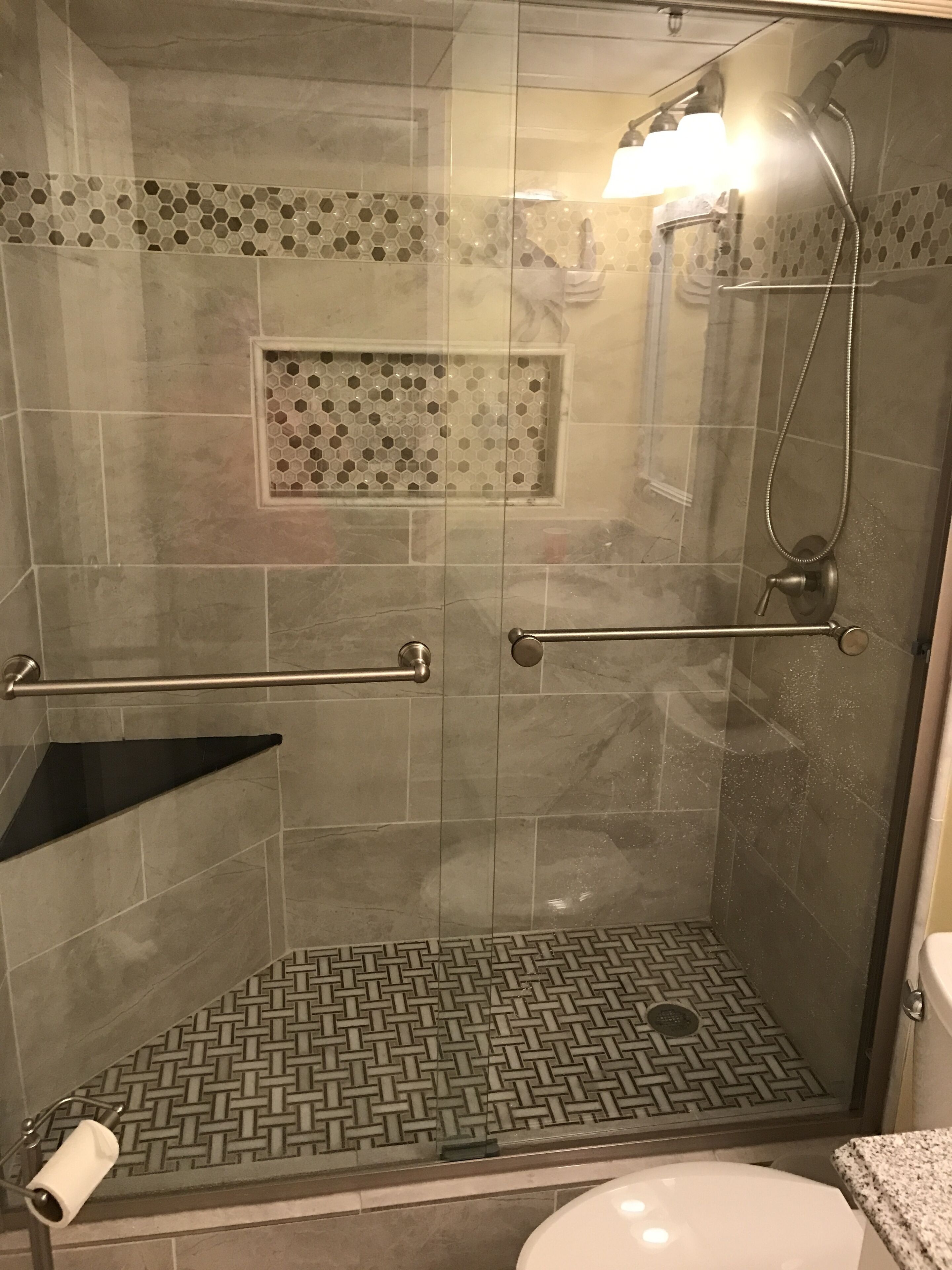 A shower area with a glass door, a handrail, a tiled floor, and a toilet visible to the right.