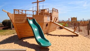 A wooden pirate ship play structure with a slide on a sandy beach. - Carousel Oceanfront Condo w/ Stunning Ocean & Bay Views! (Ocean City)