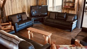 Un salon chaleureux avec deux canapés en cuir noir, une table basse en bois et un téléviseur.