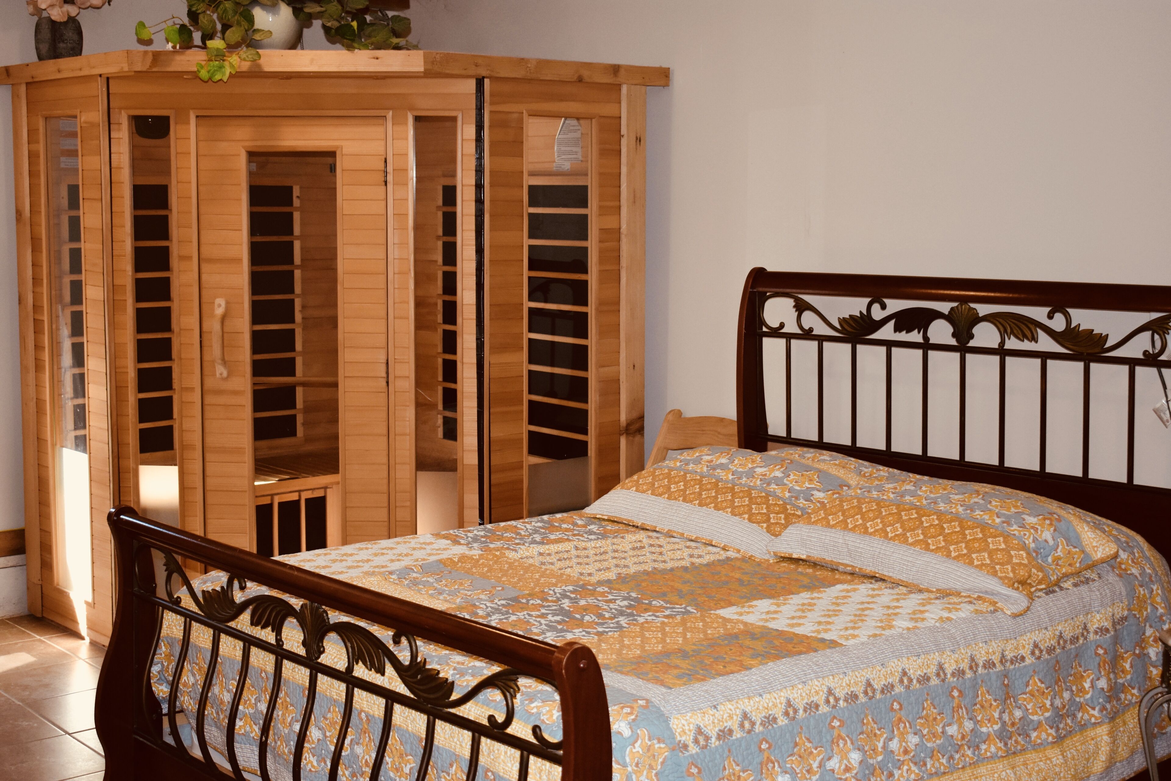 A bedroom with a wooden wardrobe, a bed with patterned bedding, and a decorative headboard.