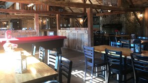 L’intérieur est de style rustique, avec des poutres en bois, un mur en pierre et un coin bar doté d’un comptoir rouge. Des tables et des chaises sont disposées pour les repas.