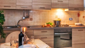 A modern kitchen with wooden cabinets, a gas stove, a sink, and a dining area set for a meal. - IL RIFUGIO DI ELA 'Apartment Garden. (Furore)