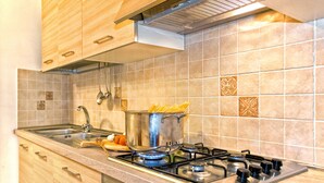 A kitchen with a gas stove, a pot on the stove, a sink, and wooden cabinets. - IL RIFUGIO DI ELA 'Apartment Garden. (Furore)
