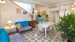 A cozy room with a blue sofa, a small table with a lamp, a dining table with chairs, and a large plant. - IL RIFUGIO DI ELA 'Apartment Garden. (Furore)