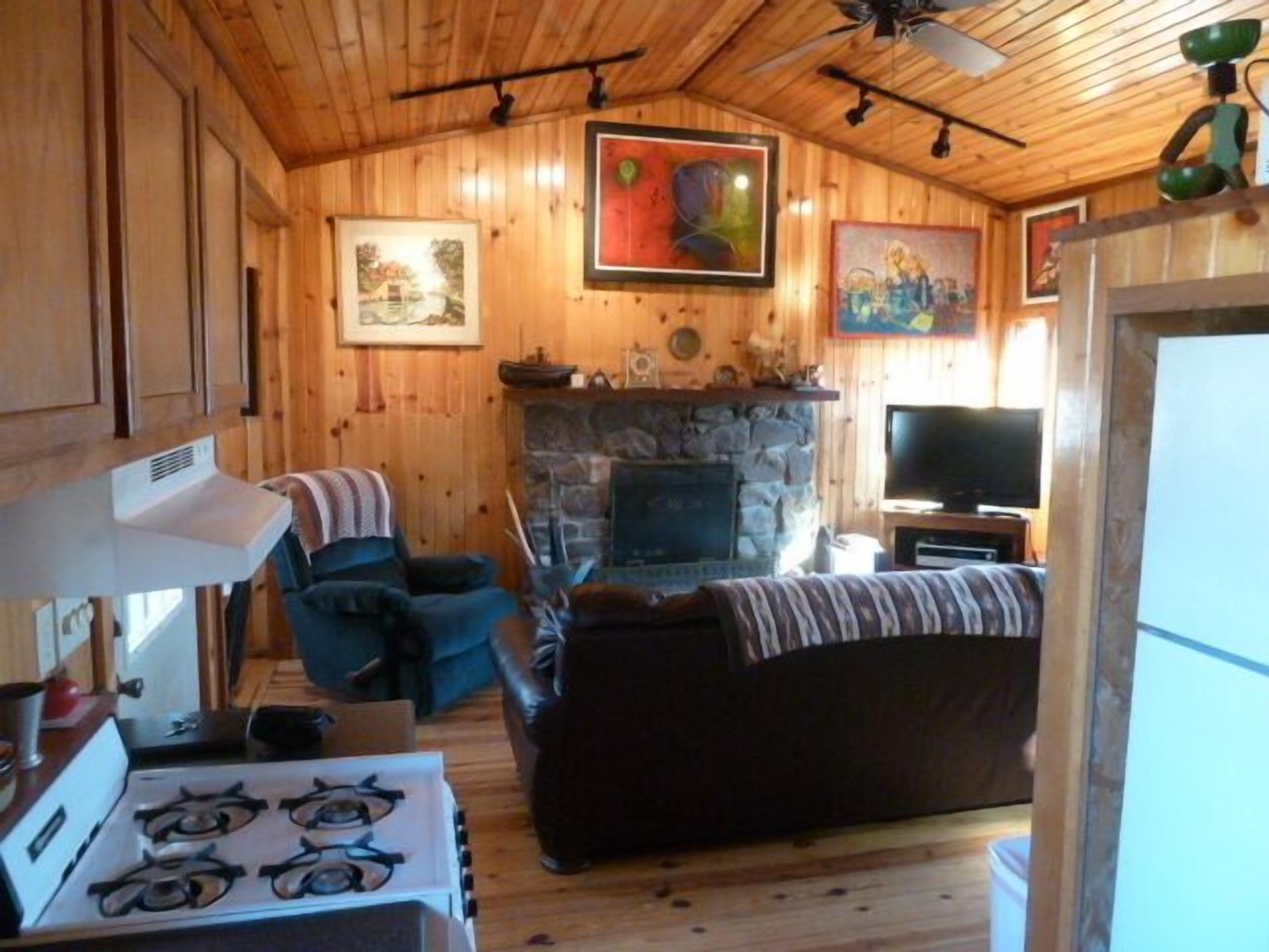 L’intérieur chaleureux d’un chalet avec une cheminée en pierre, un téléviseur et un coin repas équipé d’un poêle.