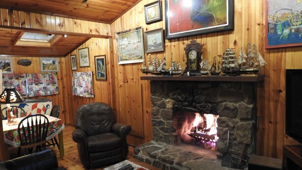 A cozy cabin interior with a stone fireplace, wooden walls, and various framed pictures.