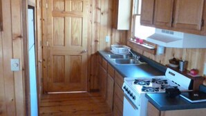 A wooden cabin kitchen with a stove, sink, and cabinets.