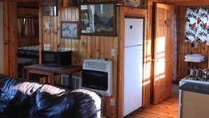 A cabin interior with wooden walls, a black leather couch, a kitchenette, and various framed artworks.