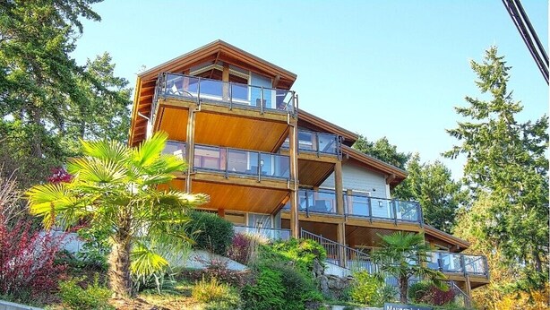 A multi-story wooden building with balconies, surrounded by lush greenery and trees. - Two Bedroom Ocean View Condo, walk to Ganges -UNIT 203 (Salt Spring Island)