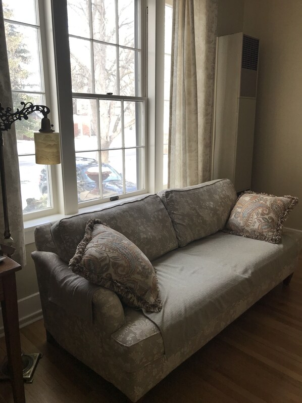A living room with a sofa, a lamp, and a window with curtains.