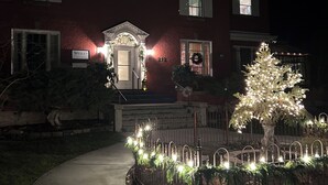 Ein zweistöckiges Haus mit roter Backsteinfassade, einer Veranda und einem beleuchteten Weihnachtsbaum.