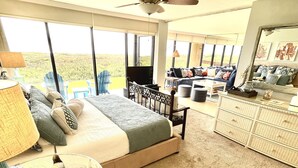 A spacious bedroom with a large bed, a ceiling fan, a view of the outdoors, a TV, and a dresser.