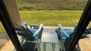 A patio with blue chairs and a table, overlooking a grassy area and a distant view.