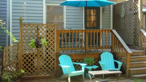 Une terrasse en bois avec deux fauteuils Adirondack turquoise, une petite table et un pot de fleurs suspendu.