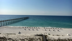 A beach with a long pier extending into the ocean, rows of beach umbrellas, and a sandy shoreline.