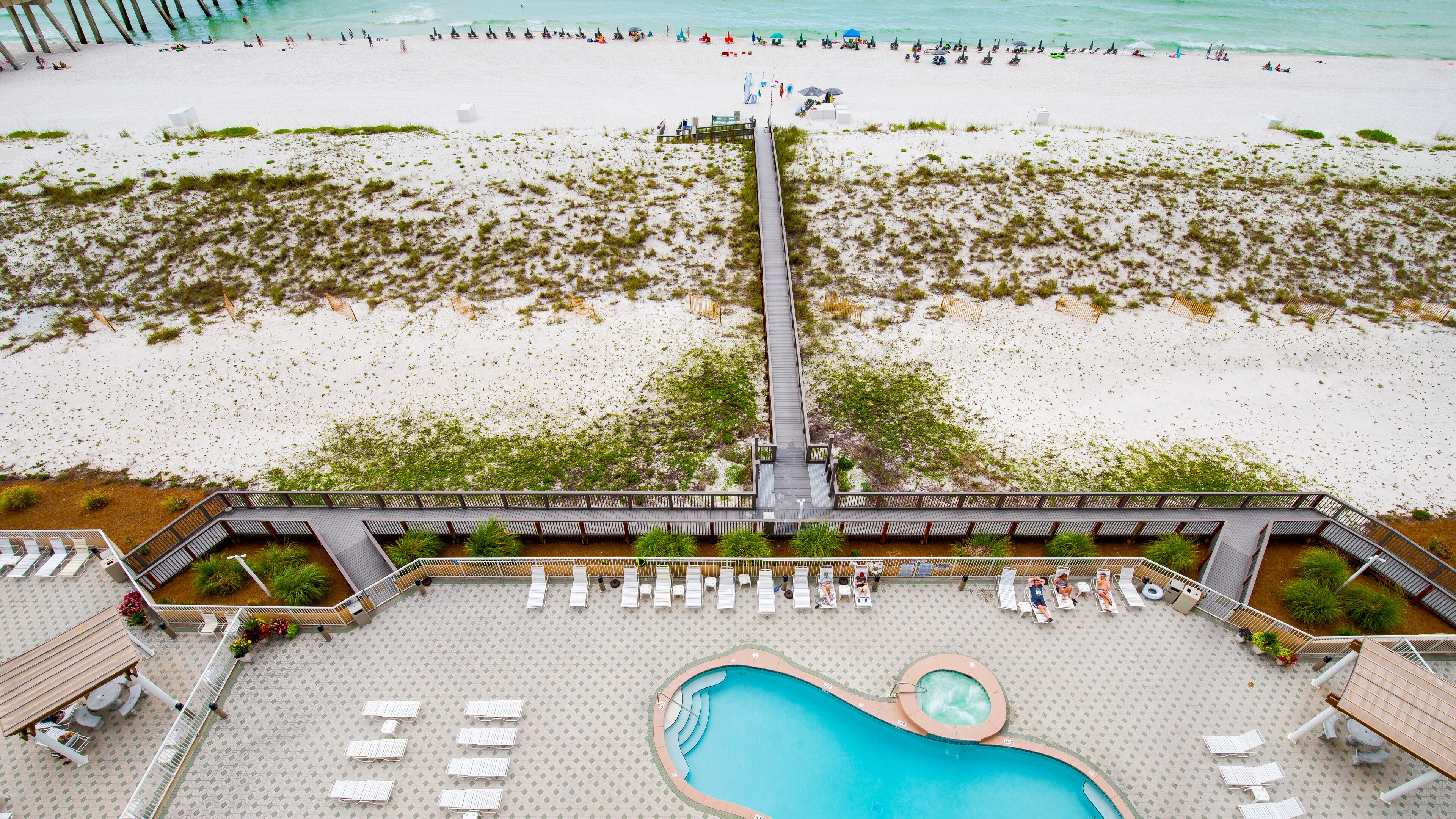 An aerial view of a beach resort with a long pier, a pool area, and beachgoers.