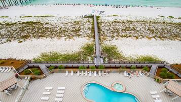 An aerial view of a beach resort with a long pier, a pool area, and beachgoers.