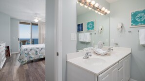 A hotel room with a balcony, a large bathroom with a vanity, and a ceiling fan.