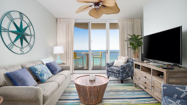 A modern living room with a sofa, armchair, coffee table, TV, and a balcony with a view of the sea.