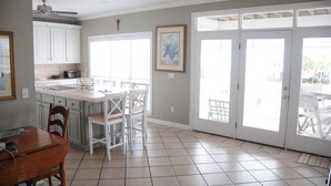 A kitchen with white cabinets, a dining table with chairs, a ceiling fan, and a large sliding glass door leading to an outdoor area. - Best First Tier House - Located in beautiful Morgantown (Gulf Shores)