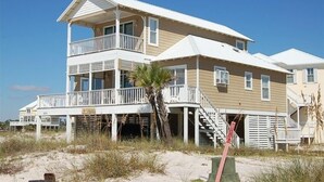A two-story beach house with a balcony, a staircase leading to the main entrance, and a sandy beach in the background. - Best First Tier House - Located in beautiful Morgantown (Gulf Shores)