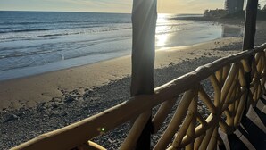 Une vue sur la plage avec une balustrade en bois, un bâtiment en construction en arrière-plan et le soleil qui brille sur l’eau.