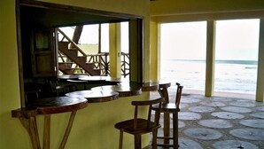 Un restaurant en bord de mer, avec des tables et des chaises en bois, une vue sur l’océan et un sol carrelé en pierre.